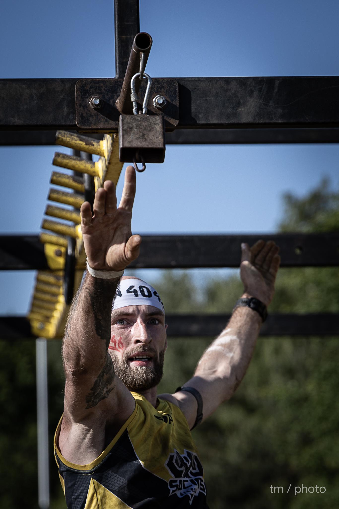 OCR athlete climbing over wall obstacle covered in mud during obstacle course race